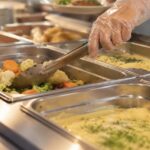 Une main servant un plat en restauration scolaire