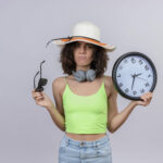 Femme avec un chapeau tenant une horloge et des lunettes de soleil