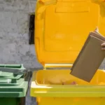 Vue sur les couvercles de poubelles de recyclage. Une personne jette un carton dans la poubelle jaune.
