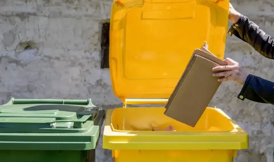 Vue sur les couvercles de poubelles de recyclage. Une personne jette un carton dans la poubelle jaune.